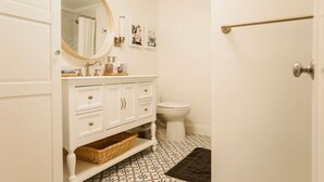 Een badkamer met een wit wastafelmeubel, een ronde spiegel, een toilet en vloertegels met een patroon.