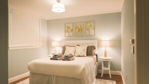 Een slaapkamer met een bed, twee nachtkastjes, een lamp, een wandlamp en een lijst met bloemen.