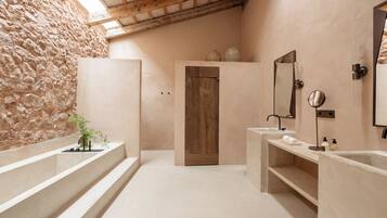 Un baño con paredes de piedra, puerta de madera y dos lavamanos con espejos.