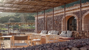 An outdoor seating area with stone walls, wooden furniture, and a pergola. - Hotel Vestige Binidufà (Ferreries)