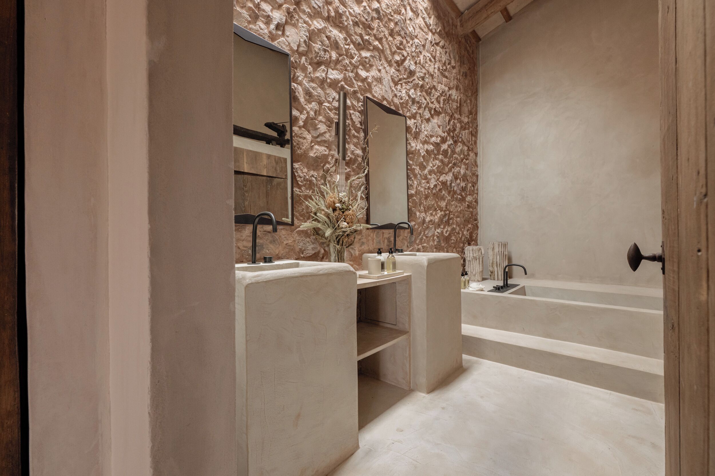 A modern bathroom with a stone wall, two sinks, a large bathtub, and a mirror.