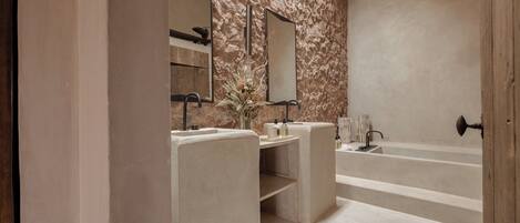 A modern bathroom with a stone wall, two sinks, a large bathtub, and a mirror.