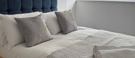 A neatly made bed with a striped blanket and two pillows, a blue upholstered headboard, and a colorful elephant painting on the wall.