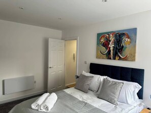 Une chambre d’hôtel avec un lit, un tableau représentant un éléphant, une porte et un thermostat.