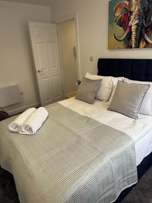 Una cama bien hecha con un edredón gris, dos almohadas grises y dos toallas blancas enrolladas.
