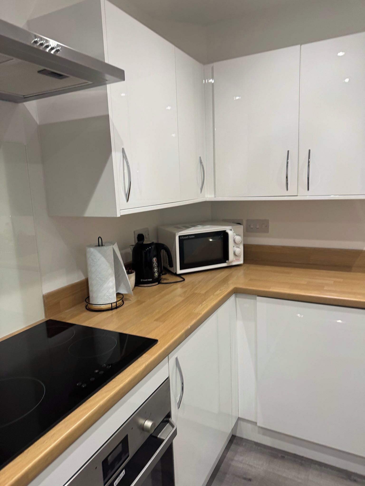 Une cuisine moderne avec des meubles blancs, un four à micro-ondes, une bouilloire et une plaque de cuisson à induction noire.