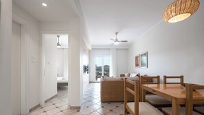 A spacious room with a dining area featuring a wooden table and chairs, a woven sofa, and a ceiling fan.