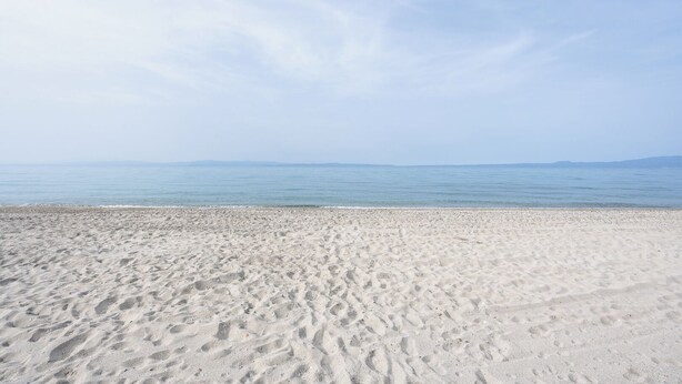 A wide sandy beach with gentle waves and a clear sky.