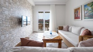 A cozy living room with a stone wall, a flat-screen TV, a wooden table, a sofa, and a view of the outdoors through a glass door.