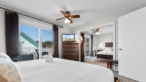 Un dormitorio con una cama grande, un ventilador de techo, un aparador, un televisor y vistas al balcón exterior.