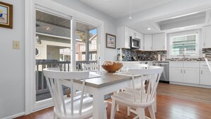 Una cocina moderna con armarios blancos, un comedor con sillas blancas y un amplio ventanal con persianas.