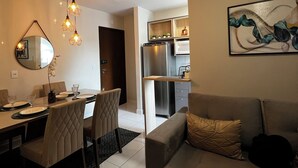 A modern living room with a grey sofa, a dining area with a table and chairs, a kitchen with appliances, and a ceiling fan. - New and Cozy Apartment! Close to the Mother Bonifácia Park and Santa Rosa Hospital. (Jardim Mariana Cuiabá)