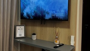 A flat-screen TV mounted on a wooden wall, a Wi-Fi sign, a small shelf with a remote, a decorative bottle, and a power strip. - New and Cozy Apartment! Close to the Mother Bonifácia Park and Santa Rosa Hospital. (Jardim Mariana Cuiabá)