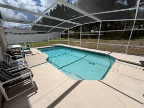 A swimming pool with a covered area, lounge chairs, and a view of trees.