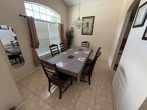 A dining area with a rectangular table, four chairs, a mirror, a potted plant, and a hanging light fixture.