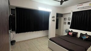 Ein Schlafzimmer mit einem Bett, einem Deckenventilator, einem Fenster mit schwarzen Vorhängen und einer Wand-Klimaanlage.