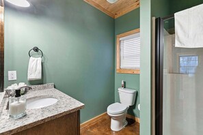Un baño con lavamanos de encimera de granito, inodoro blanco y cabina de ducha con paredes de vidrio.