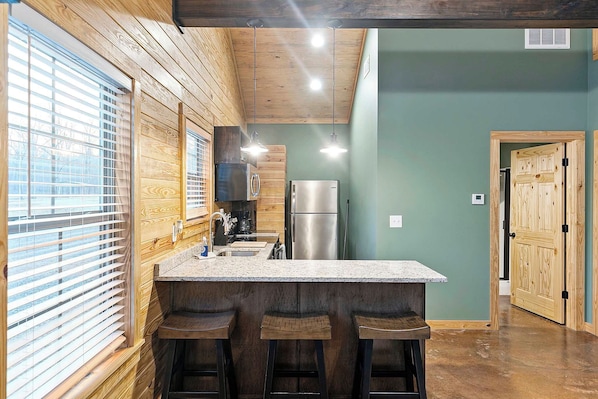 Una cocina con paredes de madera, encimera de granito y refrigerador de acero inoxidable.