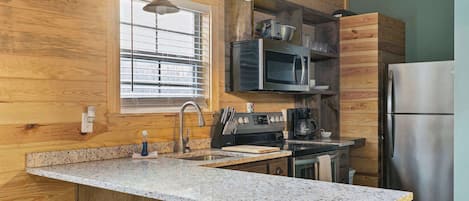 A kitchen with wooden walls, granite countertops, stainless steel appliances, and a window with blinds.