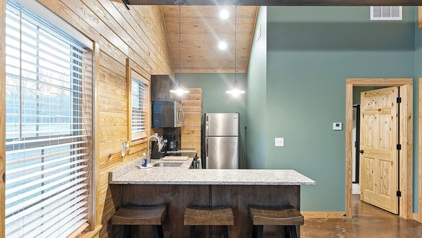 A kitchen with a wooden ceiling, a stainless steel refrigerator, and a bar area with stools.