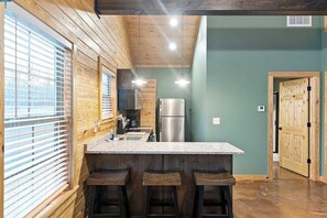 Una cocina con paredes de madera, encimera de granito y refrigerador de acero inoxidable.