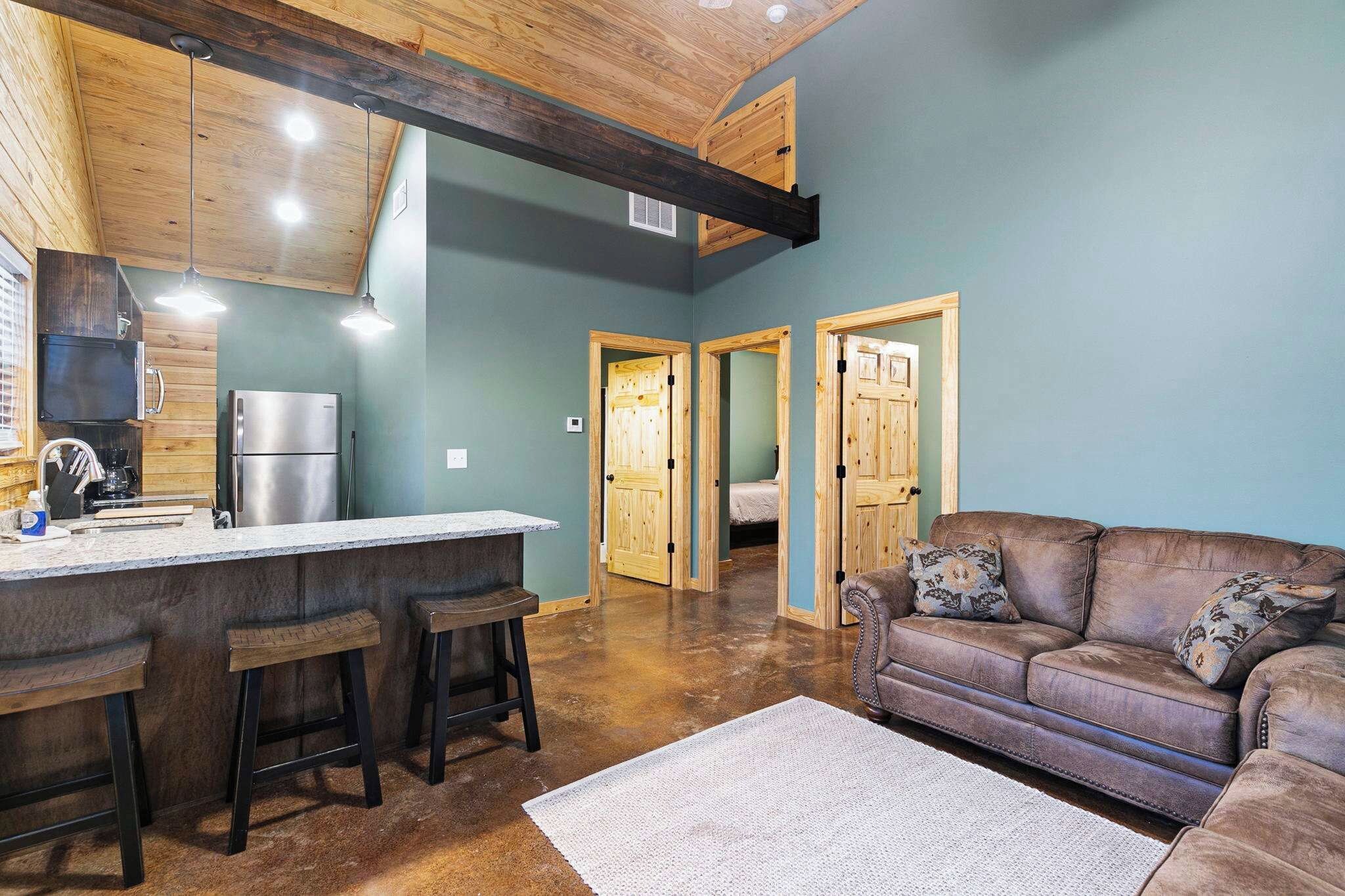 A modern kitchen with a bar area, wooden ceiling beams, and a cozy living room with a brown leather sofa.