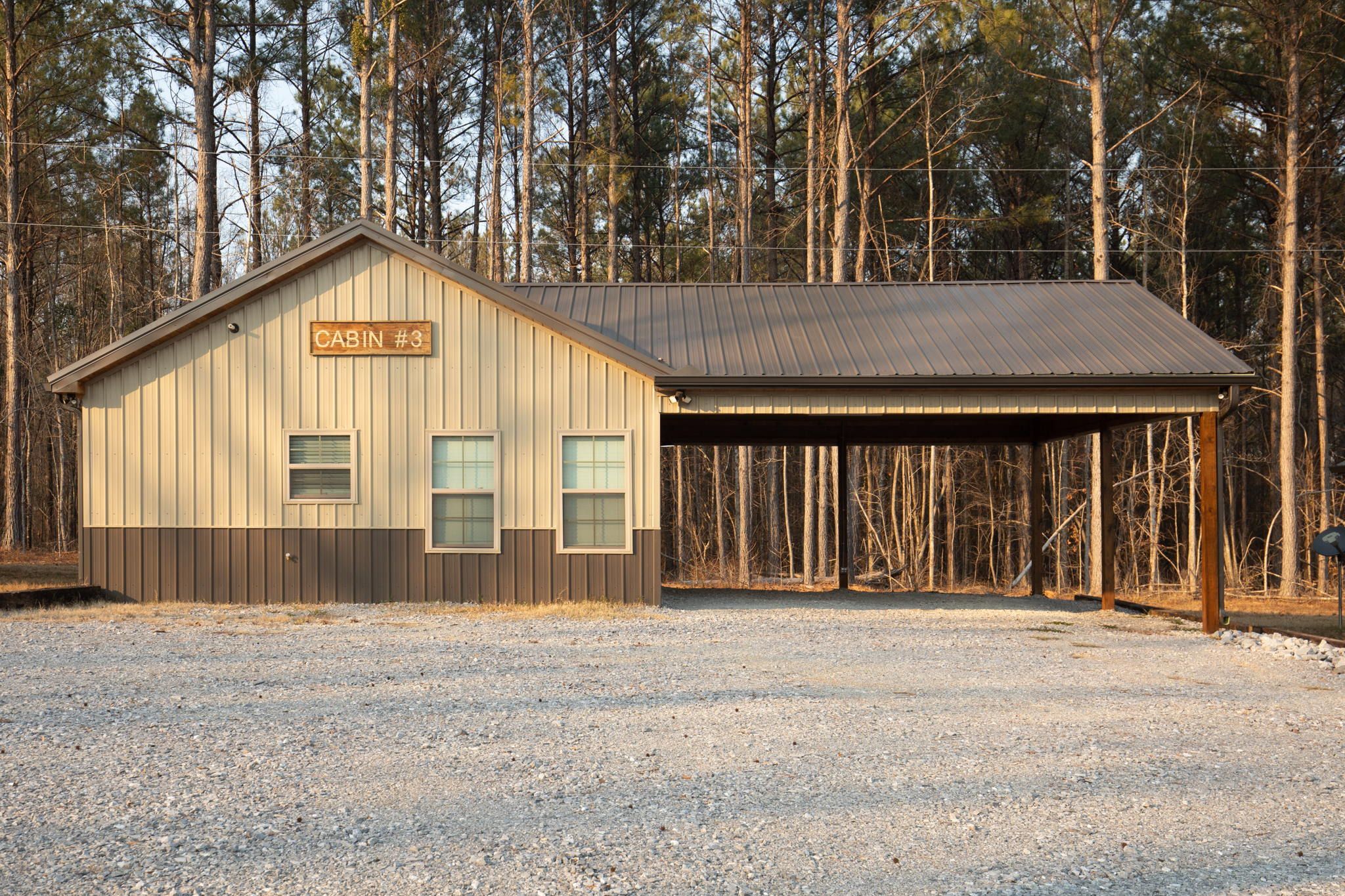 A cabin labeled "CABIN #3" with a metal roof and a covered porch area, surrounded by a forested landscape.