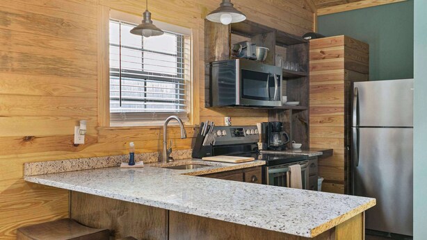 Una cocina con paredes de madera, encimeras de granito, electrodomésticos de acero inoxidable y una ventana con persianas.