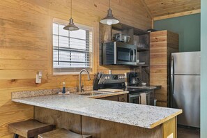 A kitchen with wooden walls, granite countertops, stainless steel appliances, and a window with blinds.
