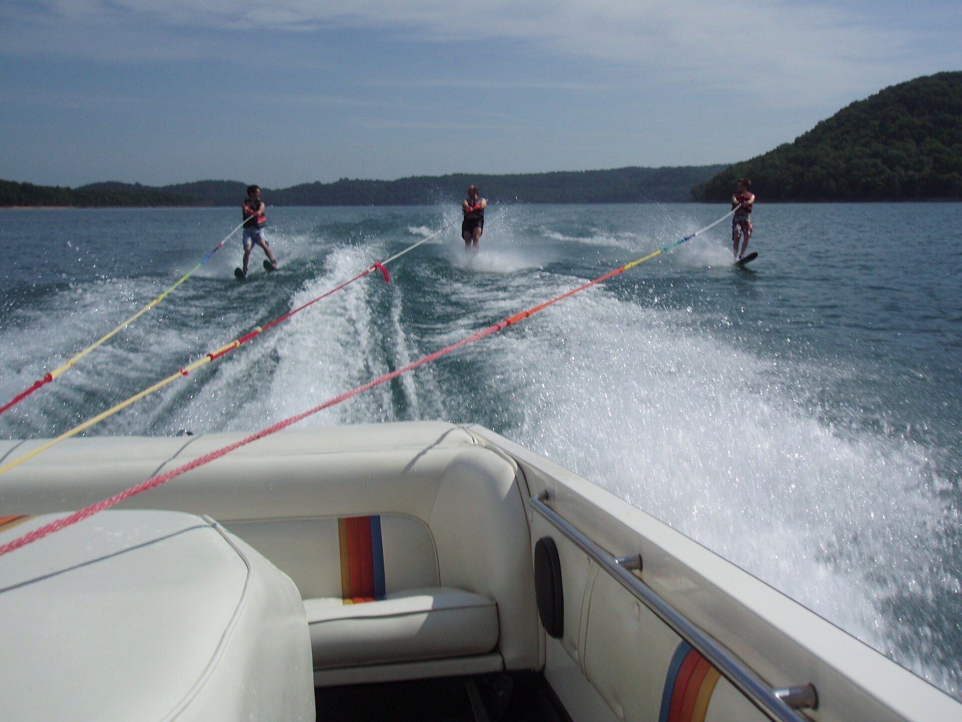 Una barca con un wakeboarder in acqua, un wakeboarder sulla barca e un wakeboarder nell'acqua.