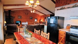 Una cocina acogedora de estilo cabaña con una mesa de comedor de madera, sillas, un refrigerador y una estufa.