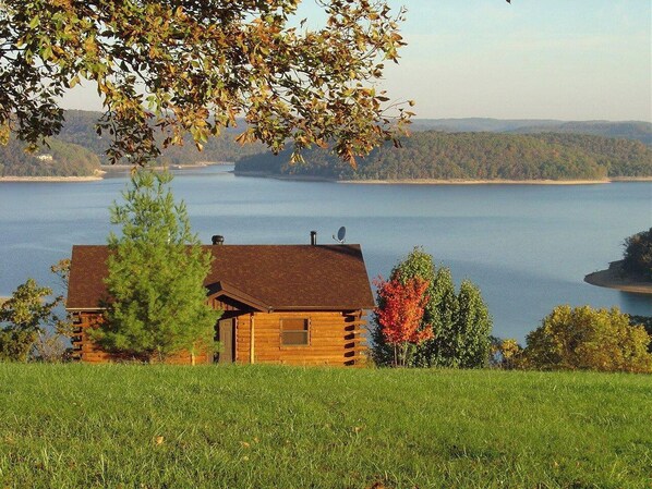 A log cabin with a view of a lake and distant hills.