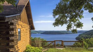 A log cabin with a deck overlooking a lake and hills.