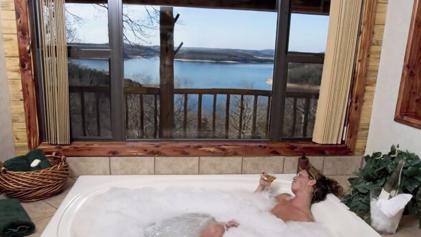 A large bathtub with a view of a lake and mountains through a window.