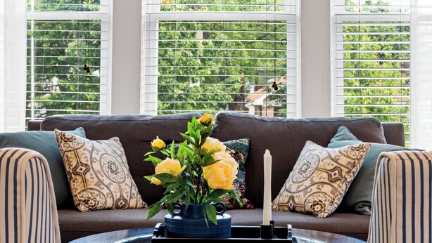 A living room with a sofa, patterned cushions, a vase with yellow flowers, and a candle on a side table. - Daily Double-Expo, UofL, Downtown, Highlands, close to track, NEW LISTING! (Louisville)