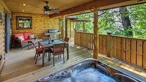 A wooden deck with a hot tub, outdoor furniture, and a view of trees.