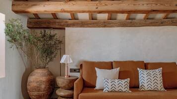 Una habitación acogedora con techo de madera, un sofá marrón, una mesa redonda negra y un jarrón grande con plantas.