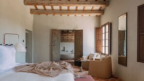 A bedroom with a large bed, a sitting area with a chair, a small table, and a large mirror on the wall. - Hotel Vestige Son Ermità (Ferreries)