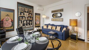 A dining area with a round table set for four, a blue sofa, and a small side table with a lamp. - Les Suites del Carmine 3 by Wonderful Italy (Genoa)