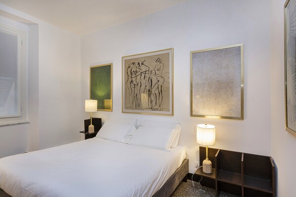 Une chambre d’hôtel avec un lit, deux tables de chevet, des œuvres d’art murales et une fenêtre.