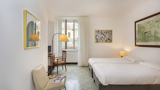 A hotel room with a bed, a desk with a chair, a lamp, and a window with curtains. - Le Suite del Carmine 1 by Wonderful Italy (Genoa)