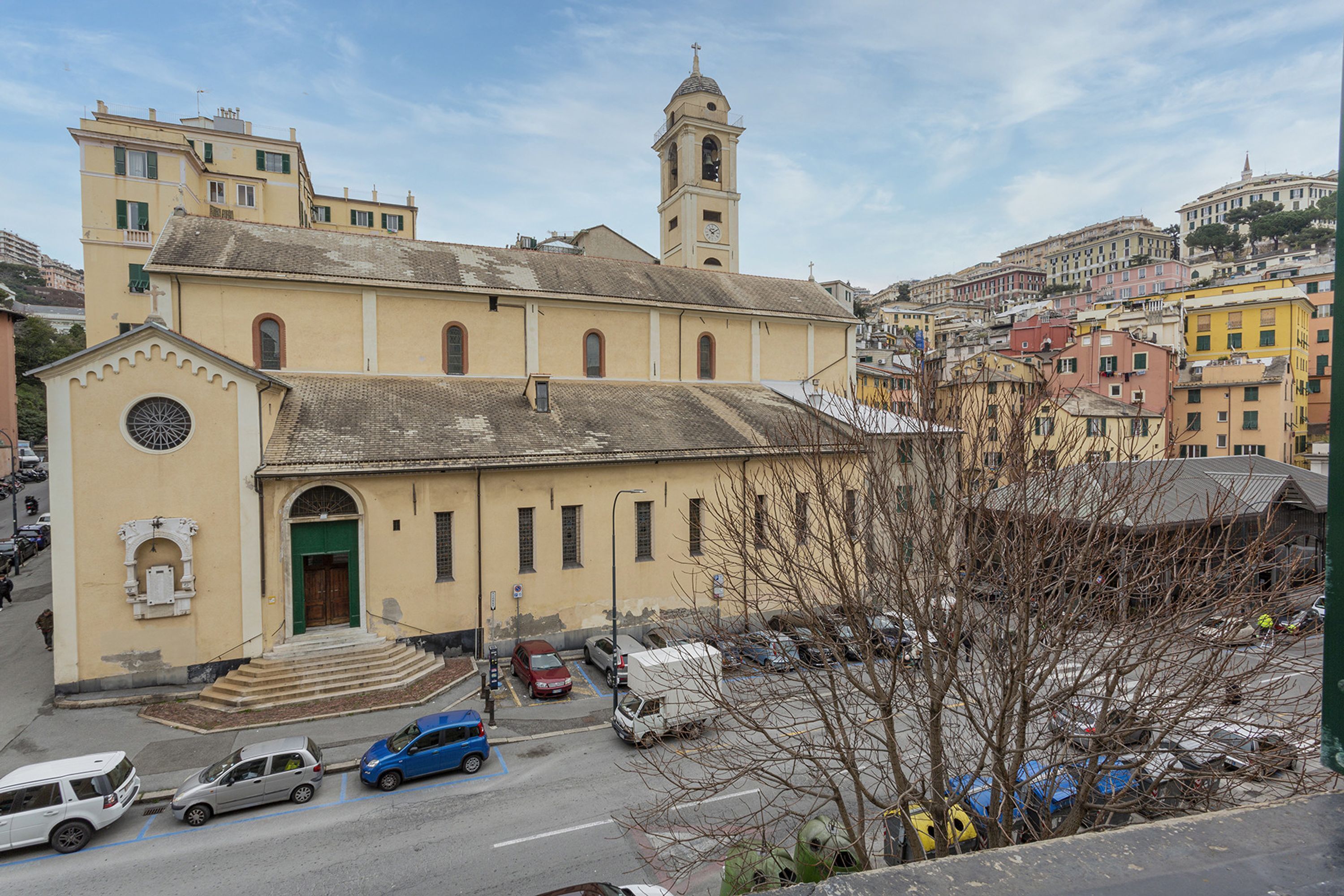 A church with a bell tower, a parking lot with cars, and surrounding buildings.