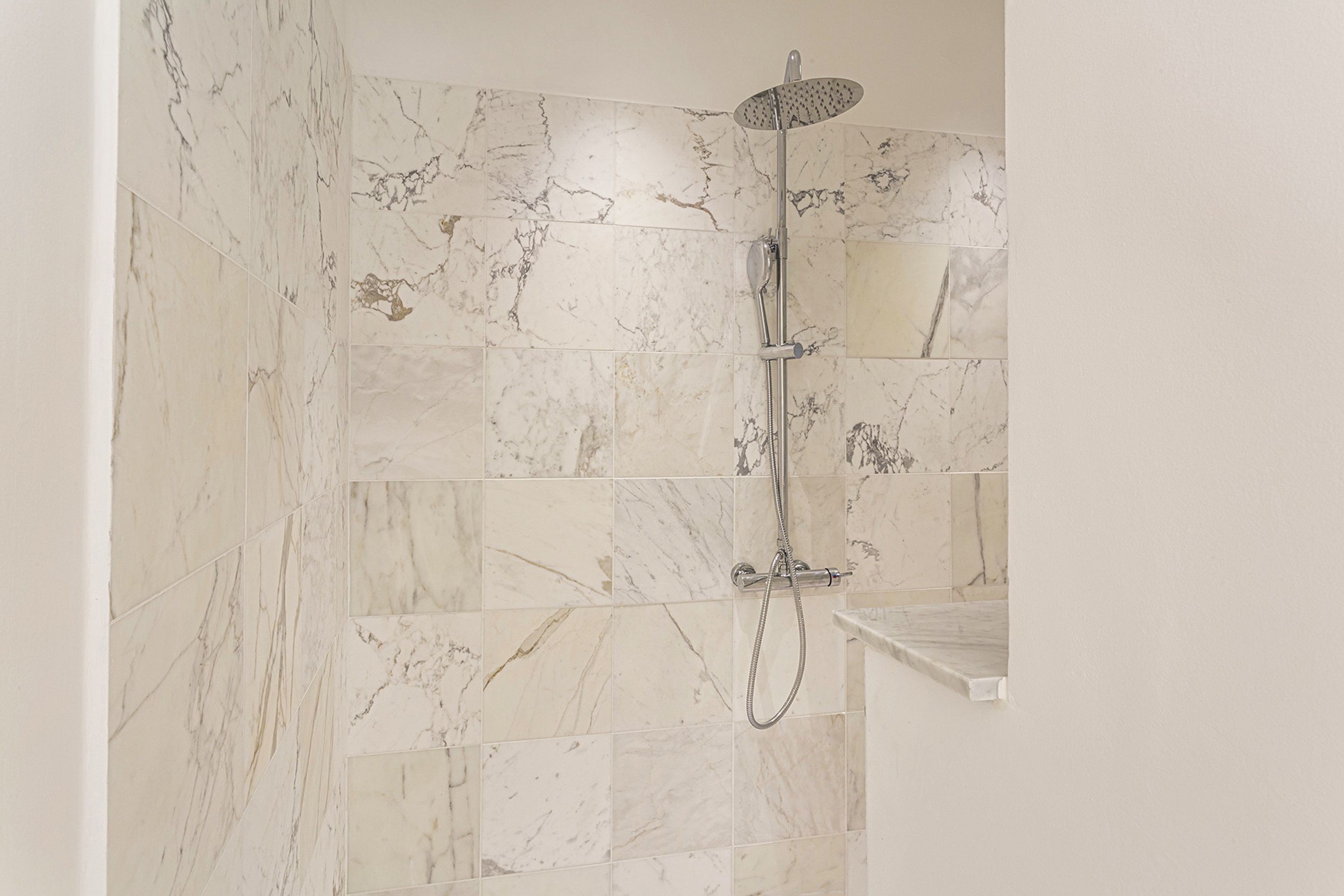 A bathroom with marble tiles and a shower with a handheld showerhead.