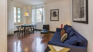 A living room with a blue sofa, a dining table with chairs, a floor lamp, and a large window with curtains. - Le Suite del Carmine 1 by Wonderful Italy (Genoa)