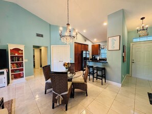 Cozy living area with a dining table for four, kitchenette, bookshelf, and flat-screen TV.