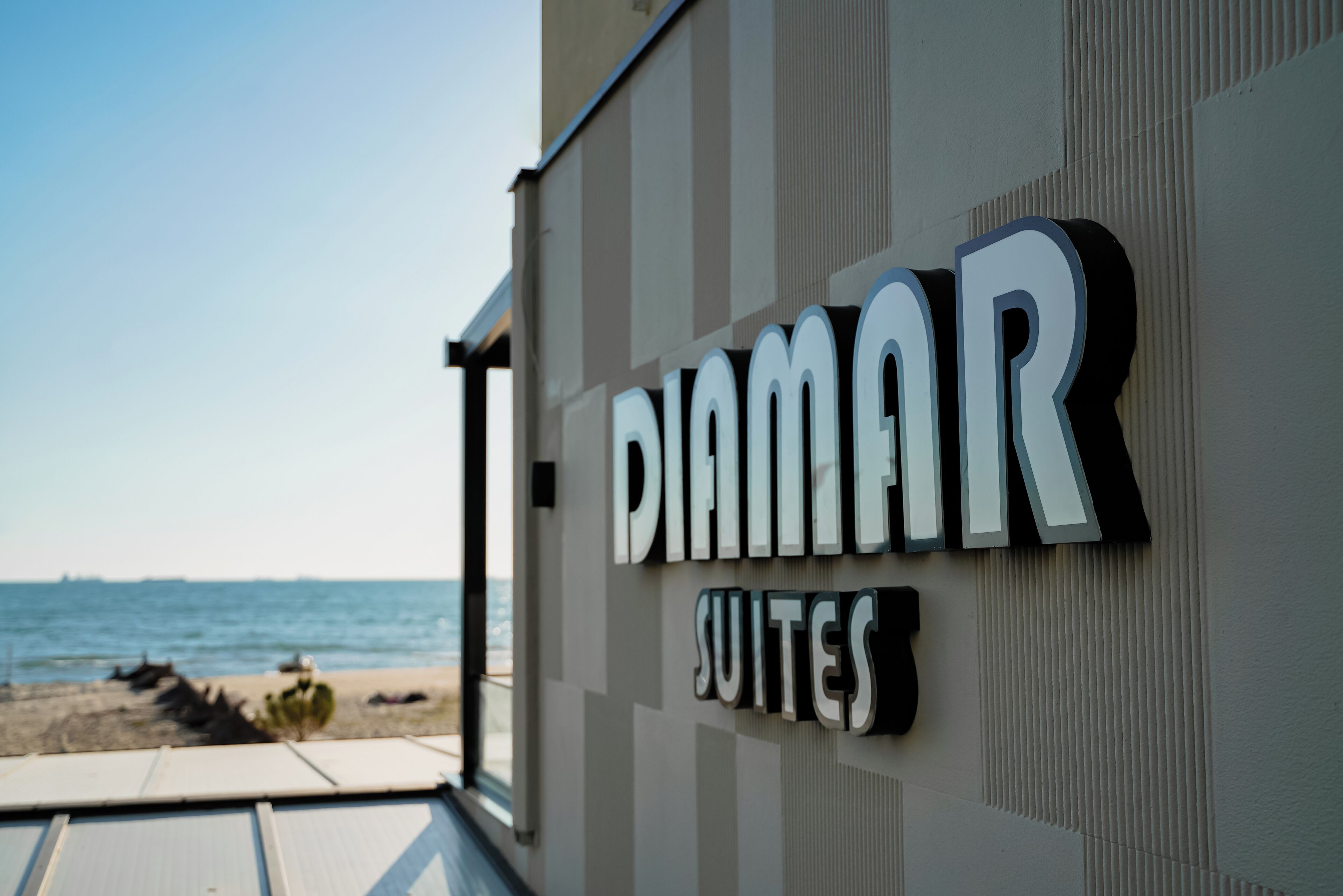 A sign for 'DIAMAR SUITES' with a view of the sea in the background.