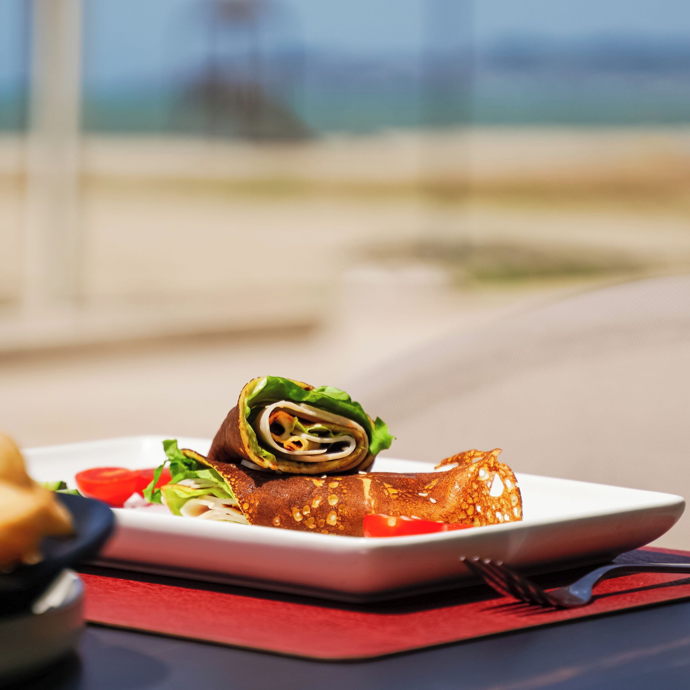 Ein Teller mit Essen, darunter ein Wrap und eine Tomatenscheibe, auf einem weißen Teller, platziert auf einer roten Servietten.