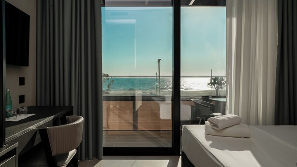 Habitación de hotel con cama, escritorio y silla, televisión y vista a la playa a través de un ventanal grande.