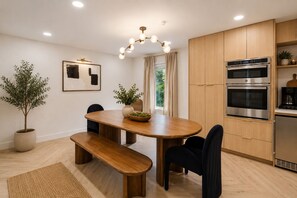 A modern kitchen with wooden cabinets, a built-in oven, and a dining area with a wooden table and bench. - Beautiful French Country Villa wt Pool & Fire-pit in marvelous Austin (Austin)