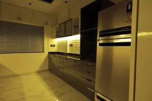 A modern kitchen with stainless steel appliances, wooden cabinets, and a large window with blinds. - Brand New Premium 3bhk furnished Place (Pune)